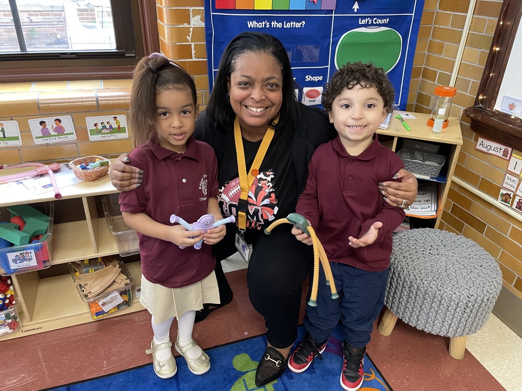 Dr. Andrea Berry-Brown, Superintendent of Schools kneeling between two young students in a classroom. Both students are holding a toy in their hands.
