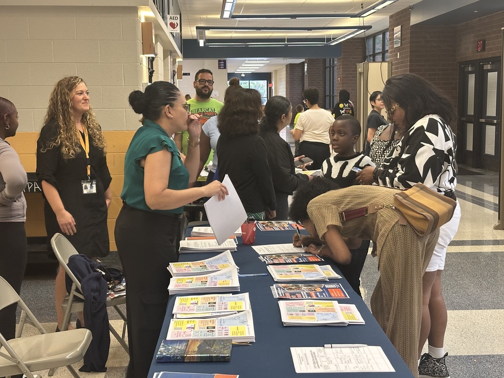 District staff members are gathered near a table with papers on it. One of the district staff members is helping a family of four.