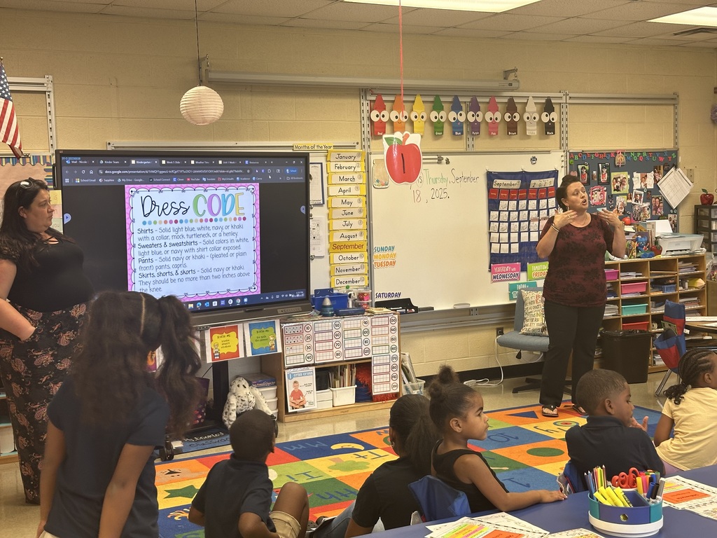 Two district staff members are presenting in front of a group of students and adults in a classroom setting.