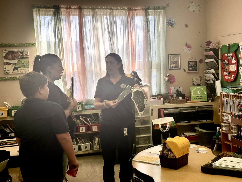 A district staff member is showing a packet to an adult and a student in a classroom setting. 