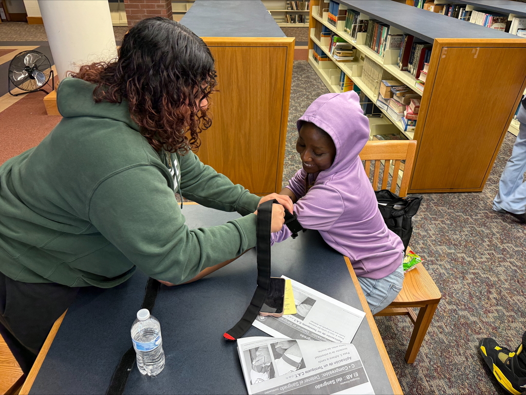 Two students are engaging in a Stop the Bleed Training in a school library.