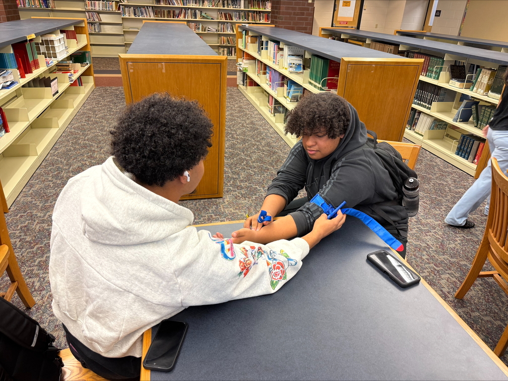 Two students are engaging in a Stop the Bleed Training in a school library.