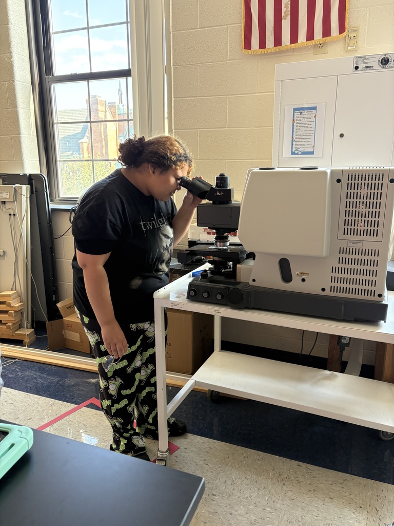 A student looking into a microscope in a classroom setting.