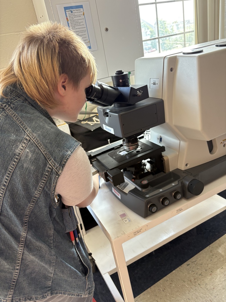 A student looking into a microscope in a classroom setting.