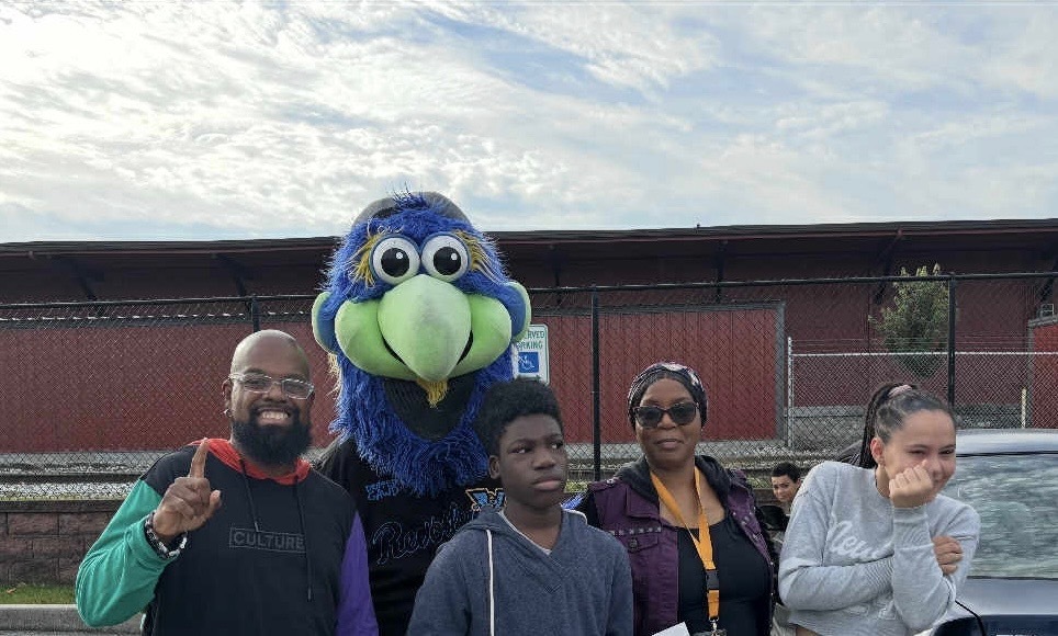 Two adults and two teenagers posing with the York Revolution mascot outside in a parking lot.