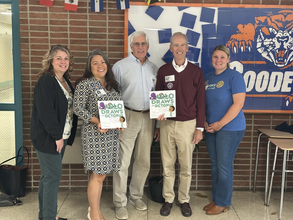 A district staff member and employees from the Rotary Club of York are standing in a school hallway at Goode PreK-8. Two of the Rotary Club of York employees are holding books in their hands.