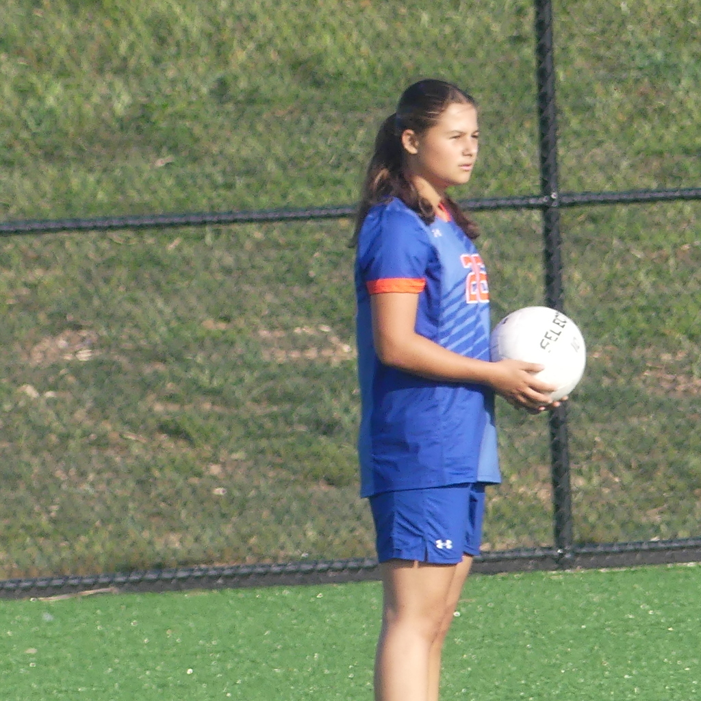York High Girls Soccer player holding a soccer ball in her hand while standing outside on the field.