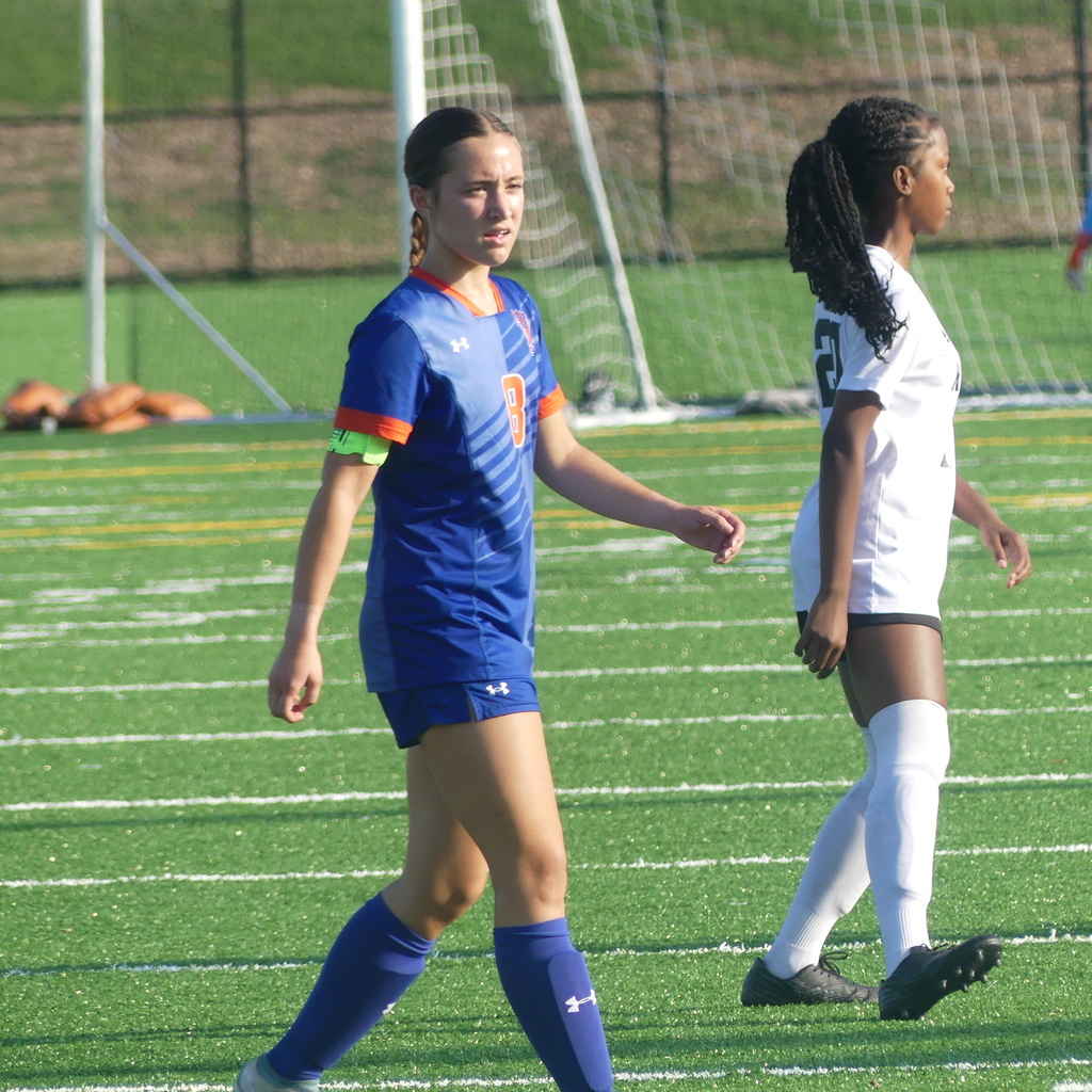 York High Girls Soccer player walking outside on the field. A soccer player from the other team can be seen standing nearby.