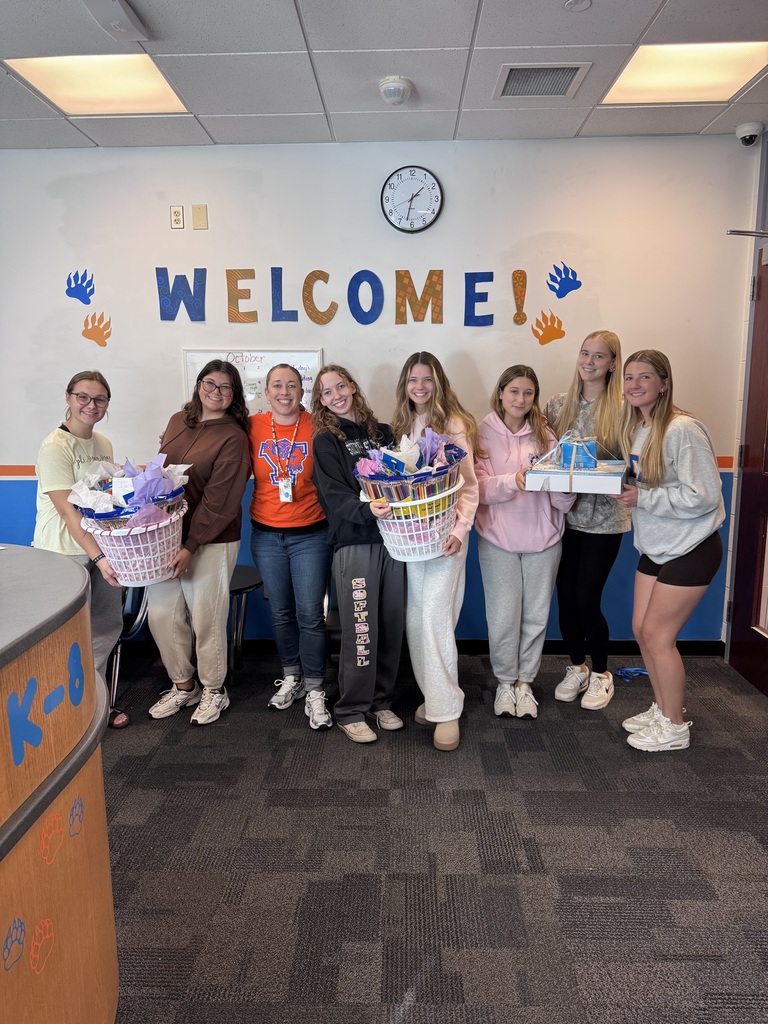 York College of Pennsylvania's Phi Sigma Sigma Sorority members and Jackson PreK-8's Assistant Principal, Ms. Philo standing in front of a wall titled "WELCOME!" in a school office area. Some of the girls are holding baskets in their hands that are filled with school supplies.