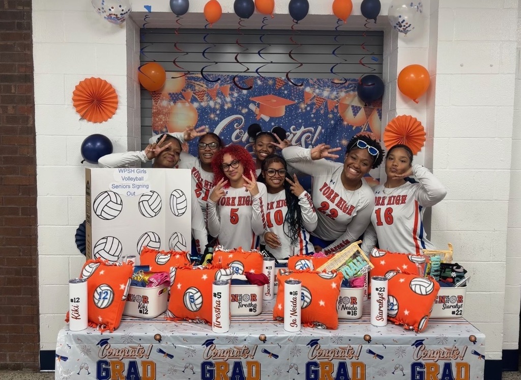 William Penn Senior High School's Seniors on the Girls Volleyball team wearing York High jerseys are posing at a “Congrats Grad” event. They are standing behind a table with gifts and volleyball-themed decorations, exuding excitement and pride.