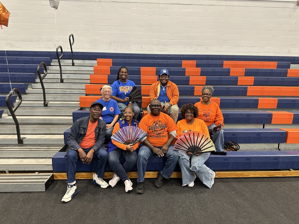 York High Alumni Dance Team sitting on orange and blue bleachers in a school gym.