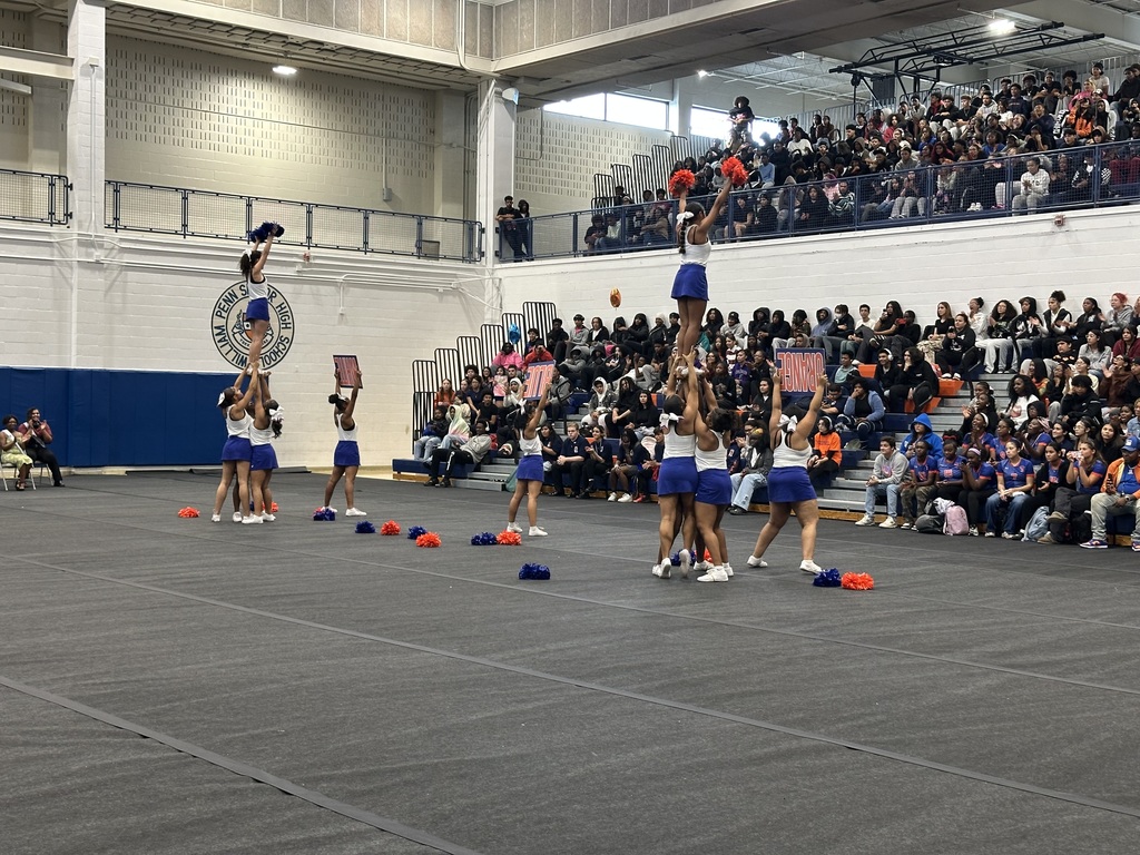 York High Cheerleaders performing a stunt on a mat in a school gym. Other people can be seen in the background observing.