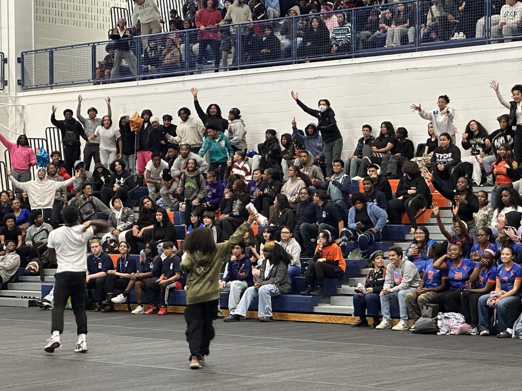 Two students throwing tshirts on a mat to a crowd of students in a school gym.