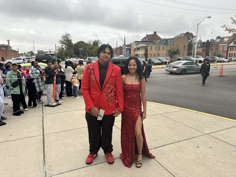 Two students are posing together outside at William Penn Senior High School’s 2025 Homecoming. Cars and other people can be seen in the background.