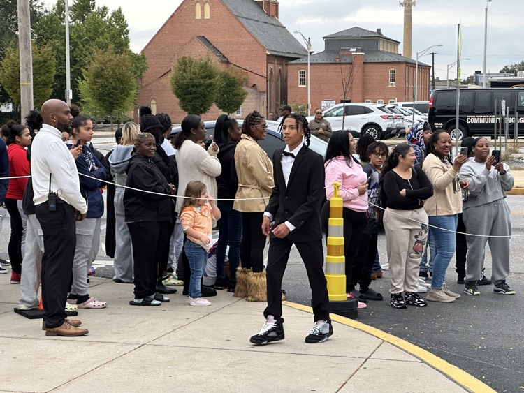 A student is walking past a crowd of people outside at William Penn Senior High School’s 2025 Homecoming. Cars can be seen in the background.
