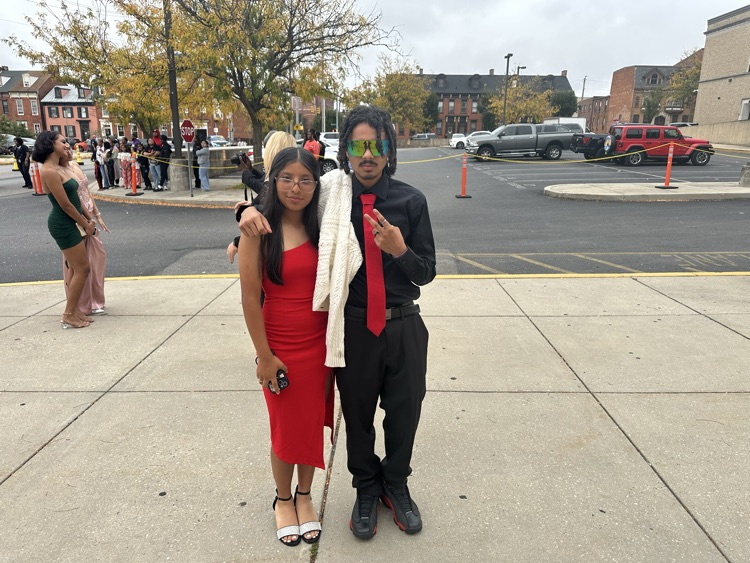 Two students are posing together outside at William Penn Senior High School’s 2025 Homecoming. Cars and other people can be seen in the background.