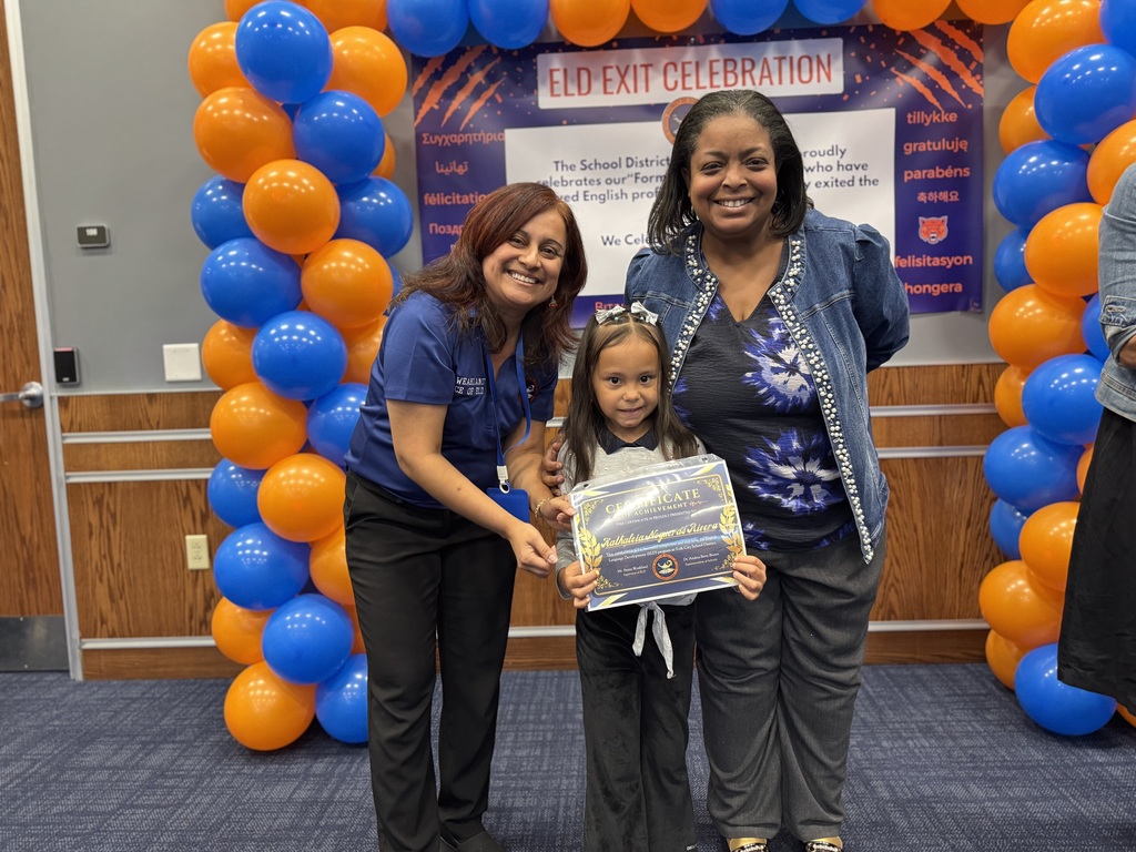 Superintendent of Schools, Dr. Andrea Berry-Brown and the district's Supervisor of ELD, Ms. Weakland posing with a student who is holding a certificate while standing in front of a banner with orange and blue balloons. The top of the banner says "ELD EXIT CELEBRATION".