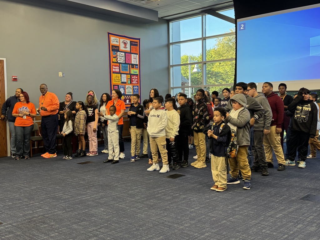 A diverse group of students and teachers standing attentively in a classroom, presenting a unified and engaged atmosphere. 