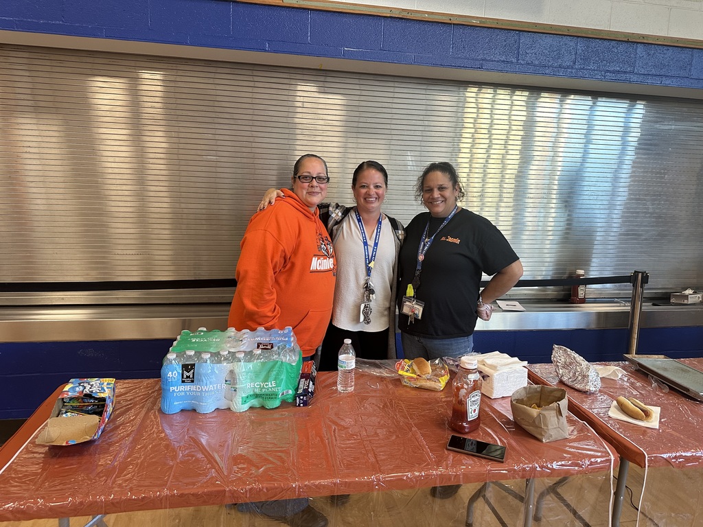 McKinley PreK-8 Principal, Dr. Ashley White standing in between two district staff members who are standing behind a table that has snacks and drinks on it. 