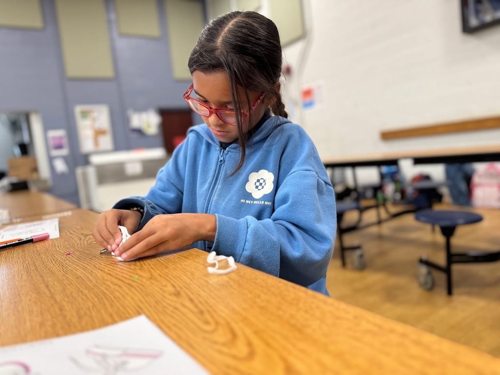 A student is sitting at a table in a school cafeteria engaging in an activity.