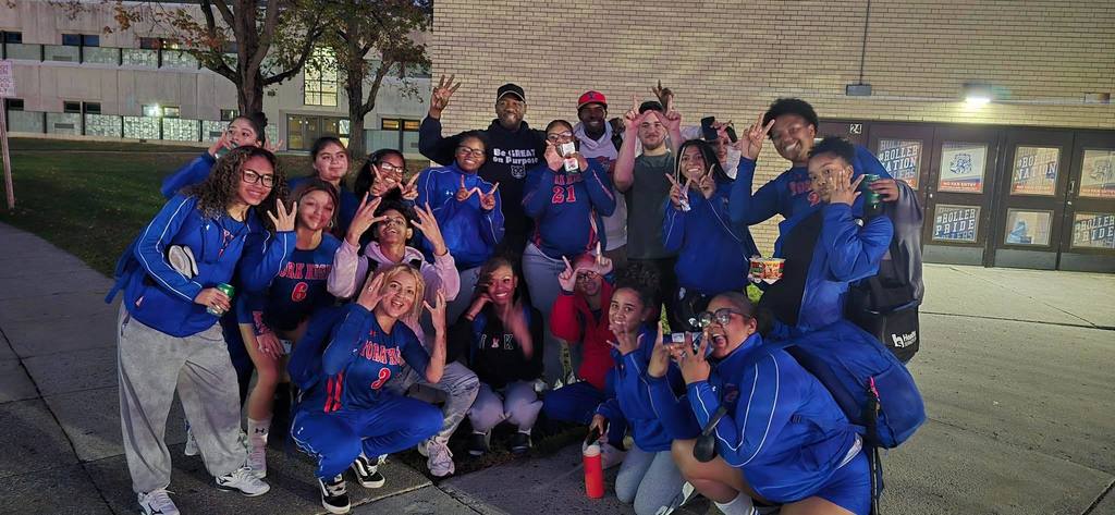 District staff and the York High Girls Volleyball team in matching blue athletic jackets posing outdoors.