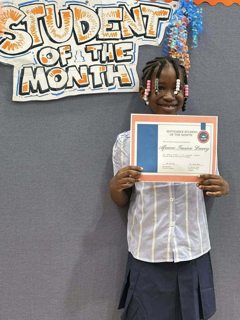 A student is standing in front of a "Student of the Month" sign, holding a certificate at Ferguson PreK-8's September Student of the Month Celebration.