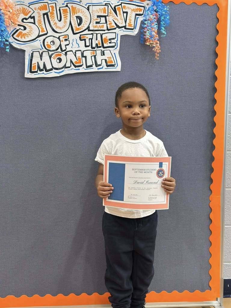 A student is standing in front of a "Student of the Month" sign, holding a certificate at Ferguson PreK-8's September Student of the Month Celebration.