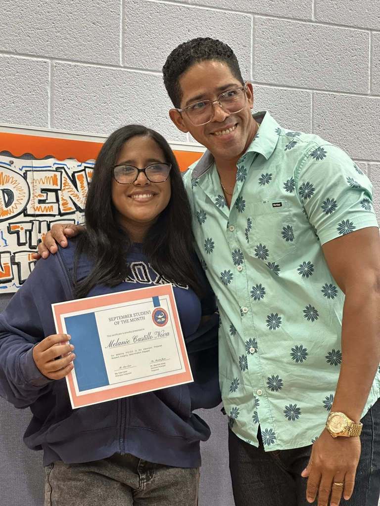 A student and an adult are smiling in front of a "Student of the Month" sign. The student is holding a certificate at Ferguson PreK-8's September Student of the Month Celebration.