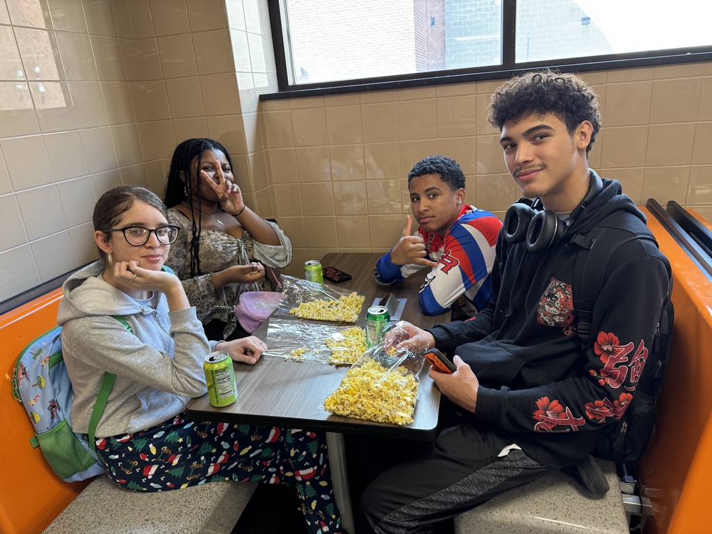 A group of students sitting at a table in a school cafeteria with bags of popcorn and soda.