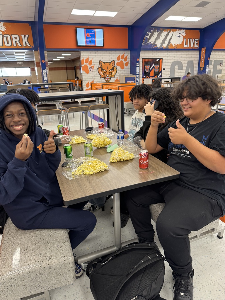 A group of students sitting at a table with popcorn and soda cans in a school cafeteria.