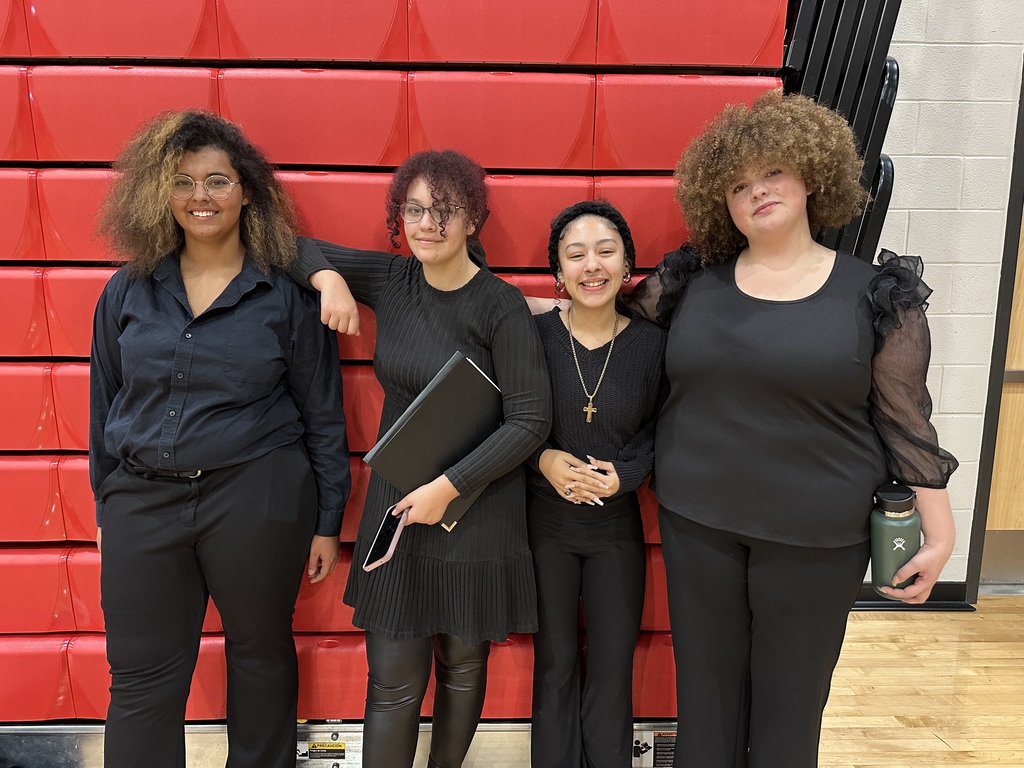 Four William Penn Senior High School students are standing in front of red bleachers in a school gym. One of the students has her arm resting on another student's shoulders.
