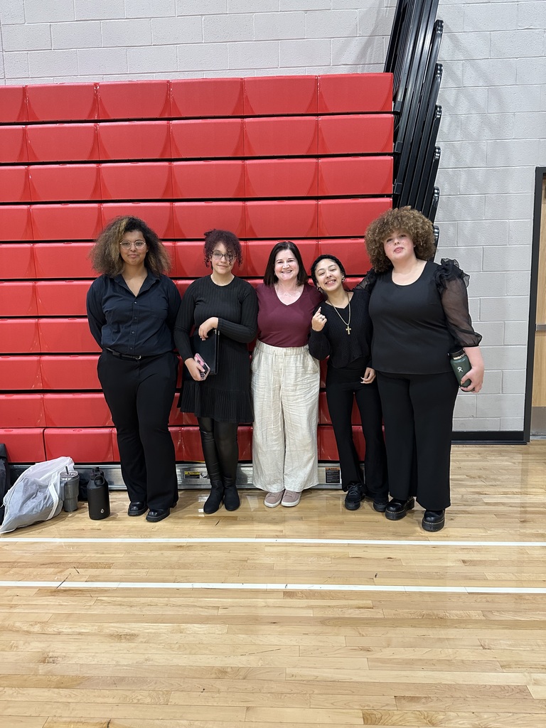 Four William Penn Senior High School students and a district staff member are standing in front of red bleachers in a school gym. Two water bottles can be seen nearby.