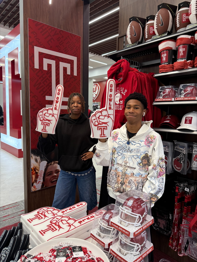 A young woman and a young man are standing in a store holding foam fingers with a letter "T." They are surrounded by sports merchandise.