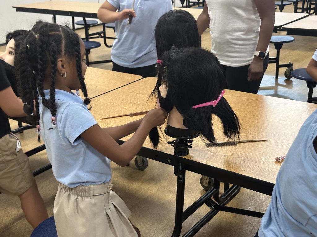 A student is working on a mannequin's head at a table, with other students working on mannequins in the background.