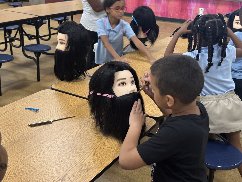 A student is working on a mannequin's head at a table, with other students working on mannequins in the background.