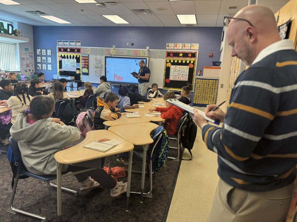 Two district staff members are observing a classroom full of students.