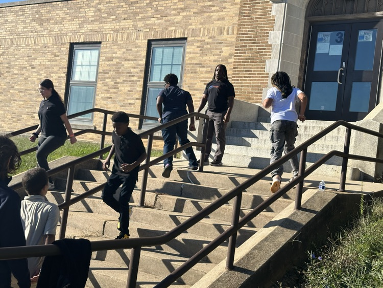 A group of students running down a flight of stairs outside while an instructor is observing nearby.