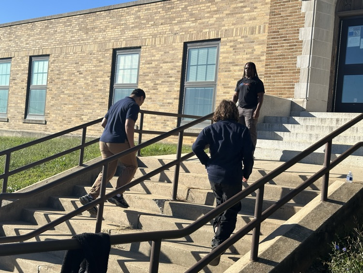 A group of students running up a flight of stairs outside while an instructor is observing nearby.