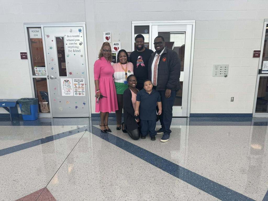 Dr. Andrea Berry-Brown, Superintendent of Schools, district leadership, and a young student are standing in a school hallway in front of an office door.