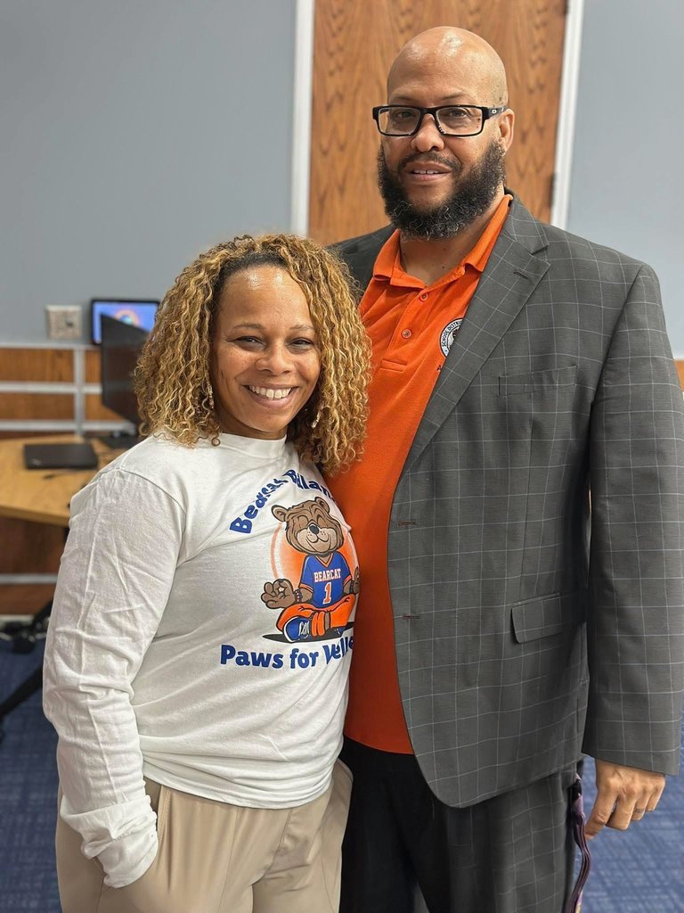 Two district staff members are standing together with their arms wrapped around each other in a conference room setting.