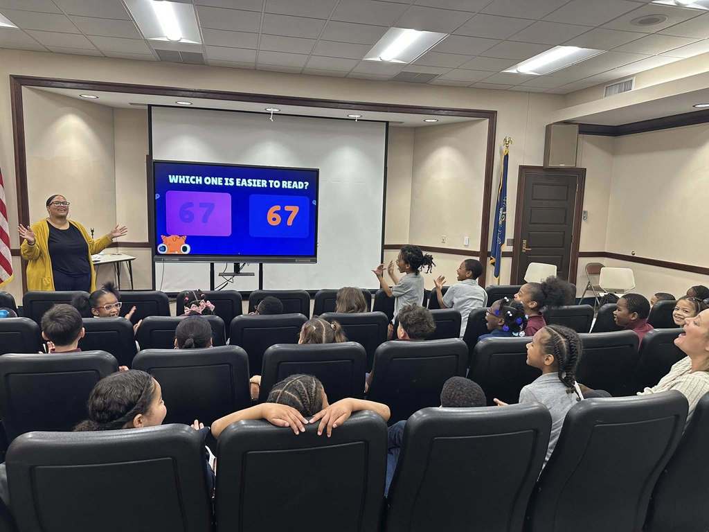 Supervisor of Communications and Marketing, ShaiQuana Mitchell is presenting to an enthusiastic group of students in a Large Group Instruction (LGI) room. The screen shows a slide asking, "Which one is easier to read?"