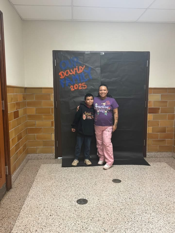 An adult and a child are standing in front of a black backdrop that says “ Our Davis Family 2025"