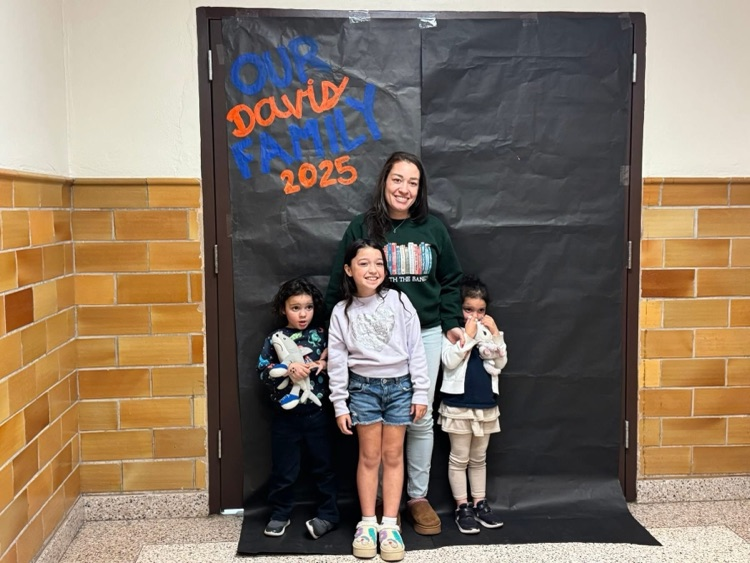 An adult and three children are standing in front of a black backdrop that says “ Our Davis Family 2025”