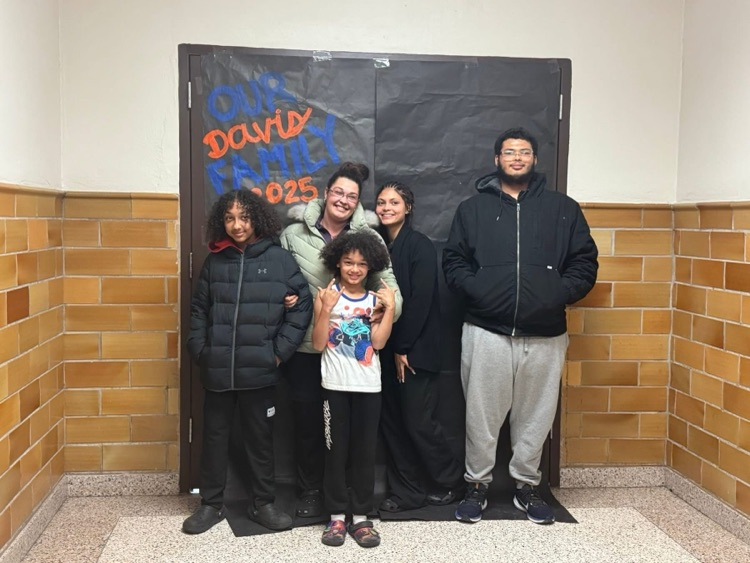 Three adults and two children are standing in front of a black backdrop that says “ Our Davis Family 2025”
