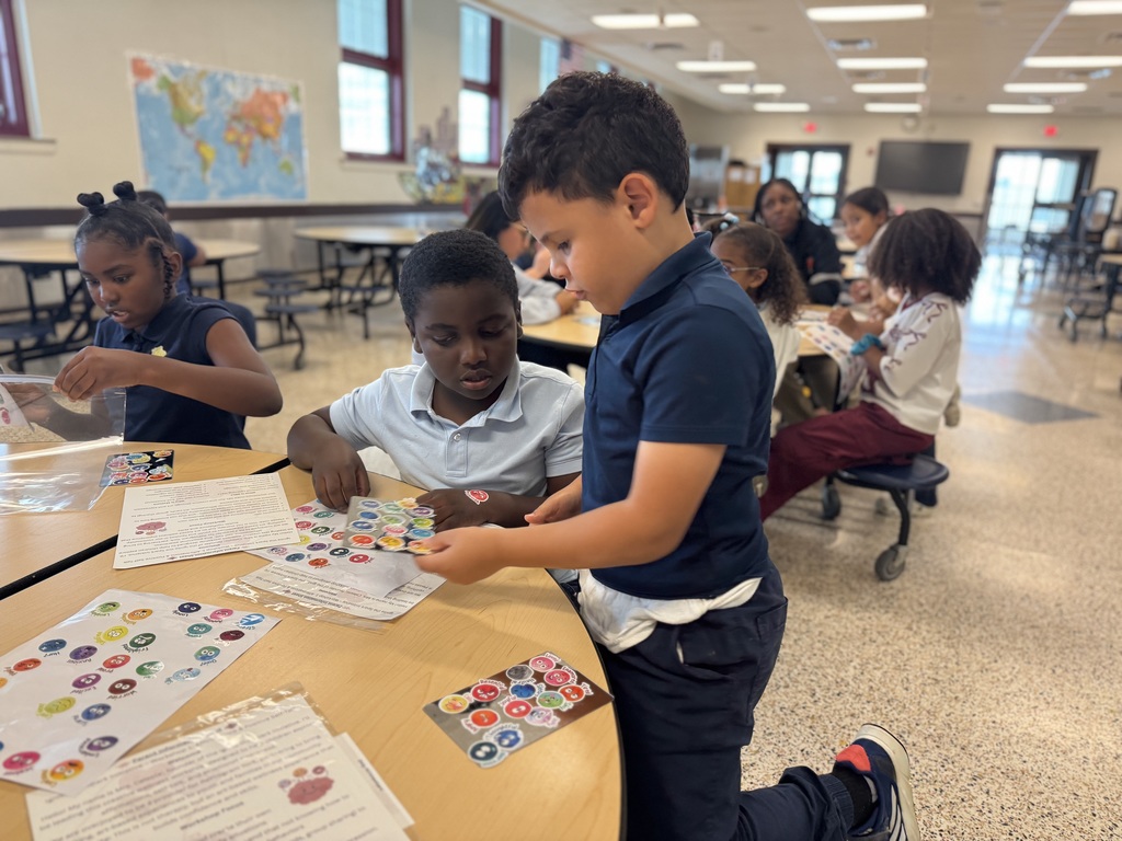 A group of students are sitting at multiple tables in a school cafeteria working on a sticker activity.