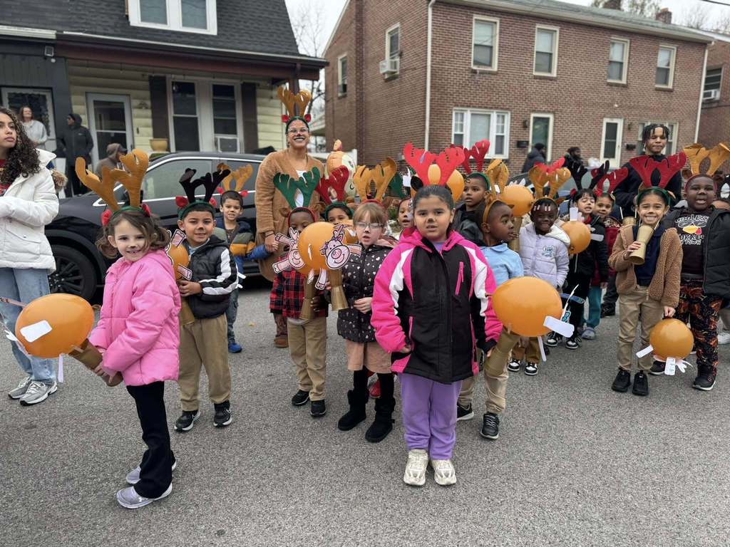 A group of district staff members and students are standing in the middle of a street wearing antler headbands, holding orange balloons and crafts.