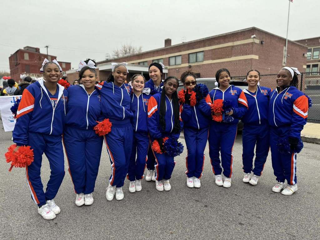 The York High Bearcat Varsity Cheerleaders are standing in the middle of a street holding orange and blue pom-poms. 