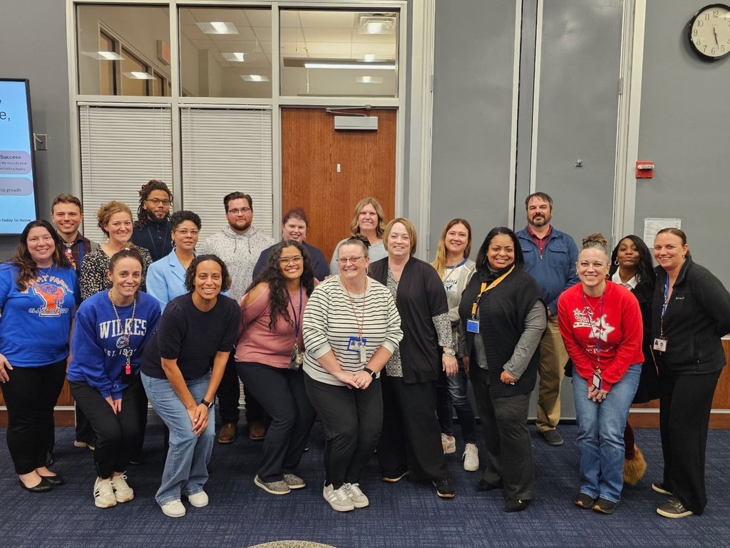 A group of eighteen district staff members standing together in a conference room. 