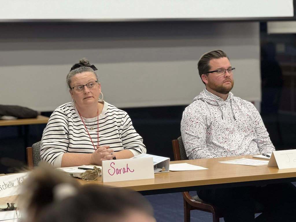 Two district staff members are sitting attentively at a table in a conference room with name tags in front of them.