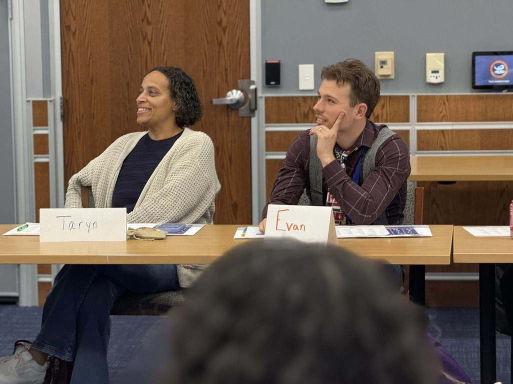 Two district staff members are sitting at a table in a conference room with name tags in front of them. 